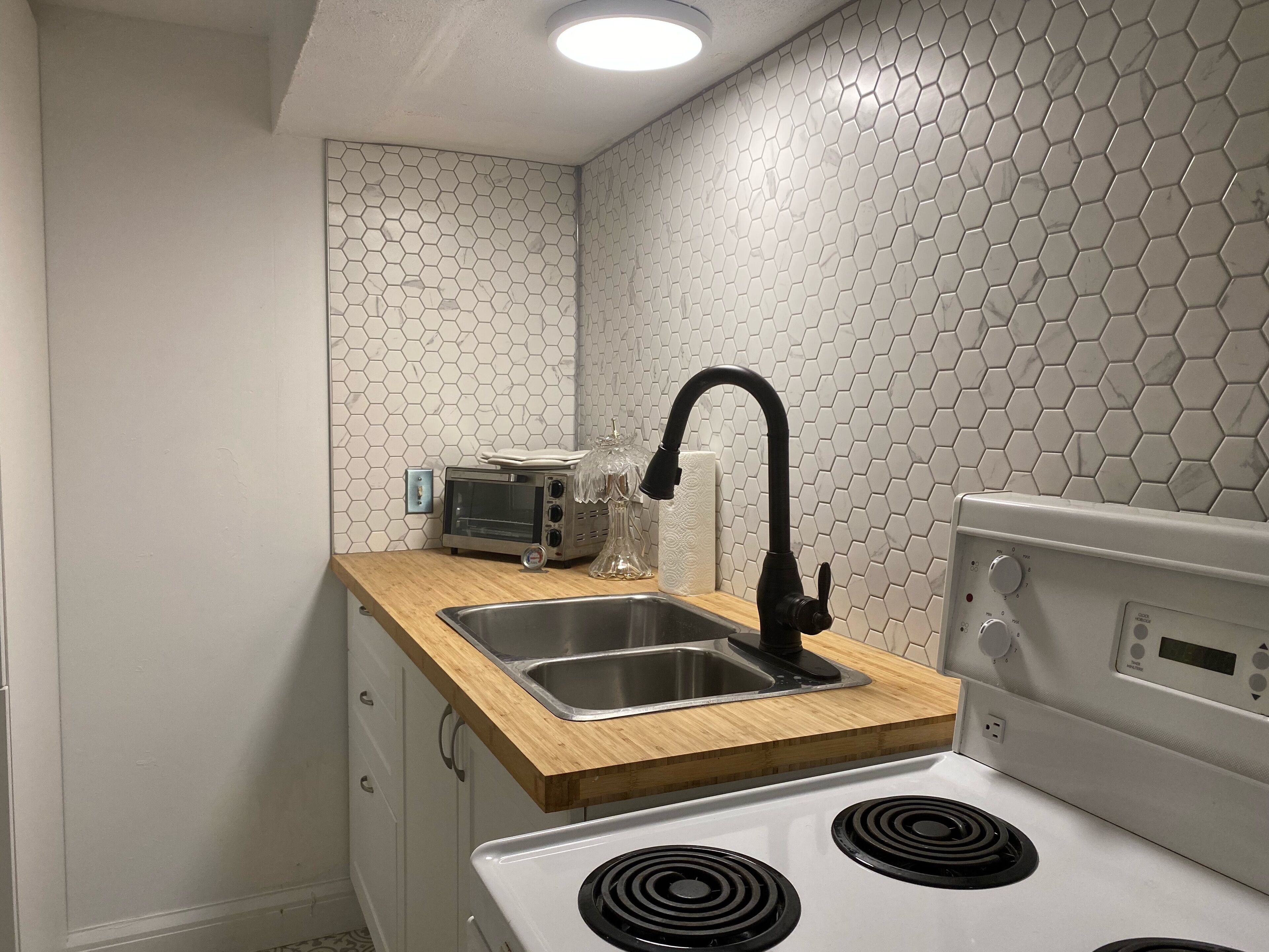 Una cocina con estufa blanca, quemadores de cocina negros, un lavamanos de acero inoxidable y encimera de madera.