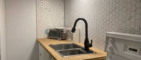 Una cocina con estufa blanca, quemadores de cocina negros, un lavamanos de acero inoxidable y encimera de madera.