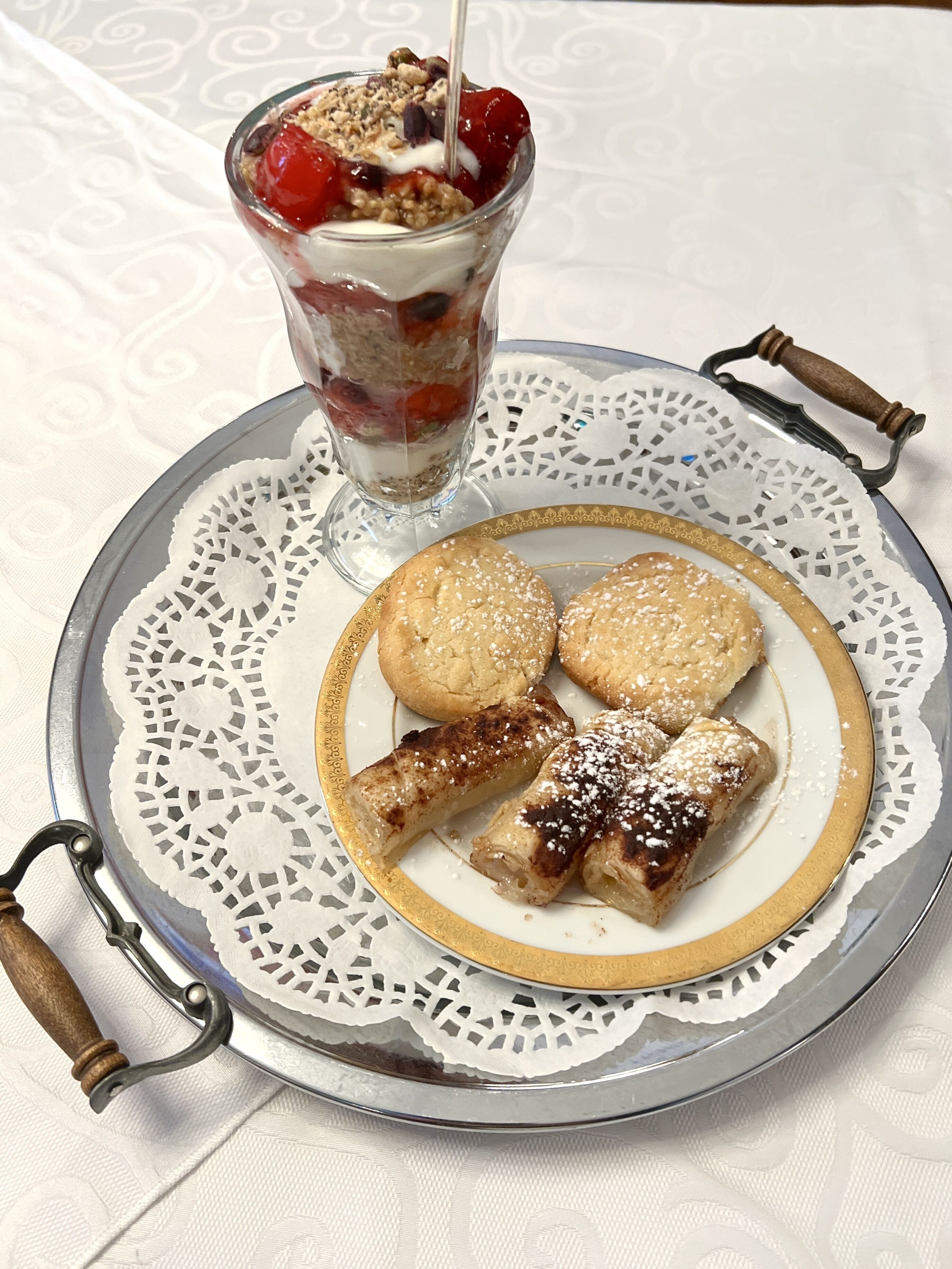 Une assiette de dessert avec une coupe de dessert en couches, des biscuits et des pâtisseries enroulées.