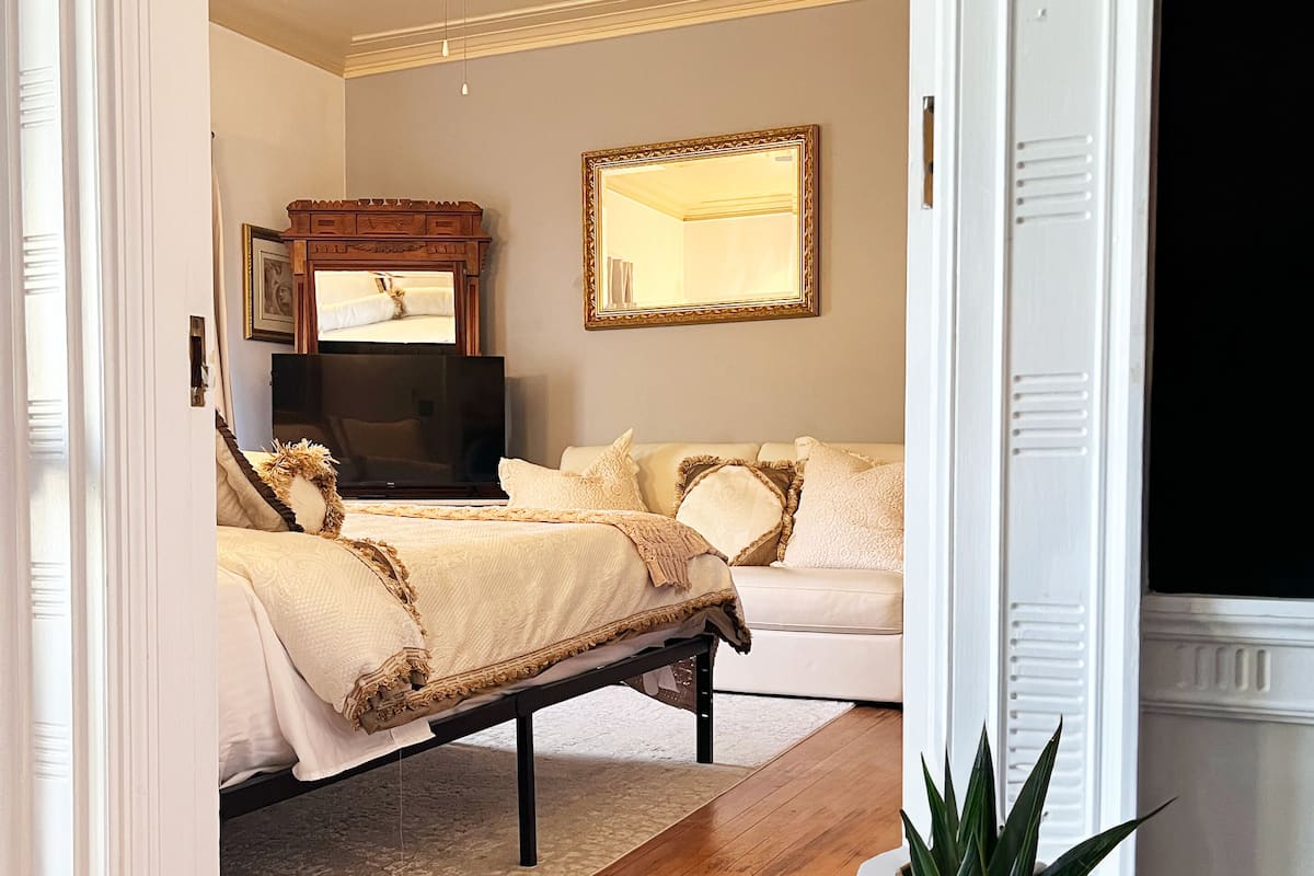 A bedroom with a bed, a bedside table with a plant, a ceiling fan, and a large mirror.