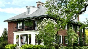 A two-story brick house with a balcony, white trim, and a chimney.