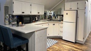 A modern kitchen with white cabinetry, a black microwave, and a refrigerator. - Clonmel Castle (Norfolk County)