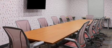 A conference room with a long table, chairs, a TV, and a projection screen.