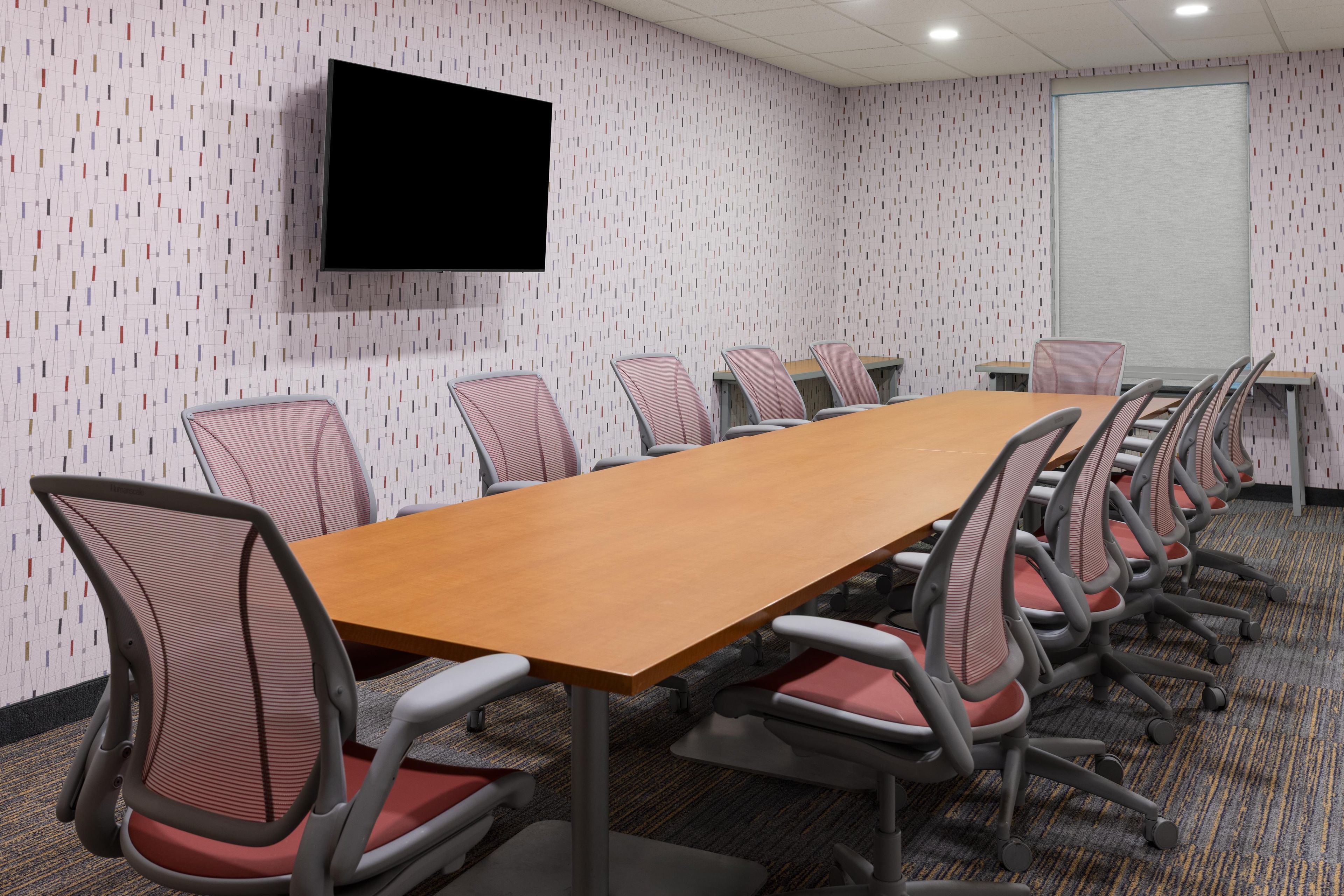 A conference room with a long table, chairs, a flat-screen TV, and a whiteboard.