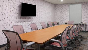 A conference room with a long table, chairs, a flat-screen TV, and a whiteboard.