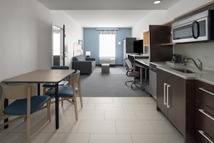 Una habitación de hotel compacta con kitchenette, zona de comedor, sofá y televisor.
