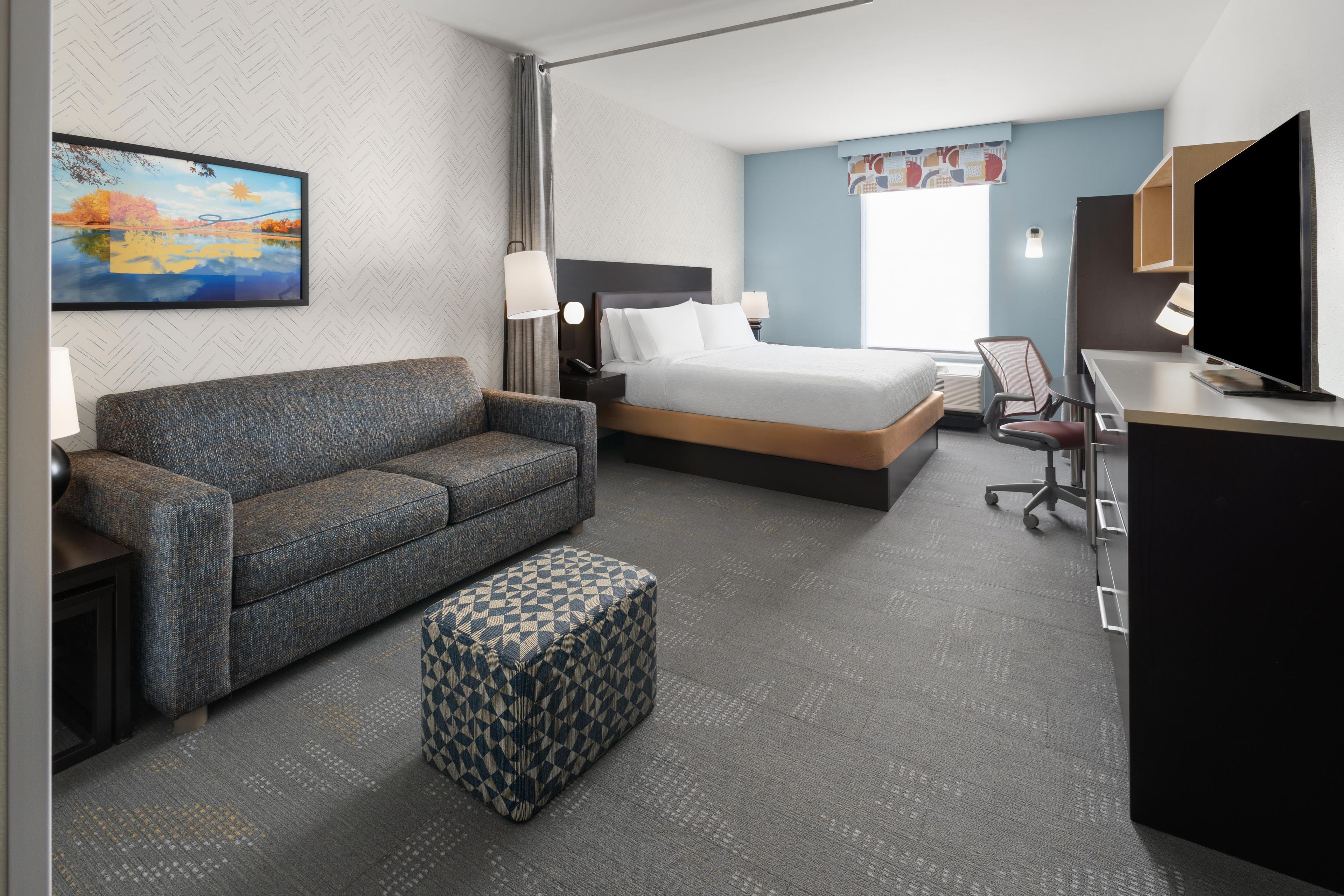 A hotel room with a bed, a sofa, a desk, and a television.