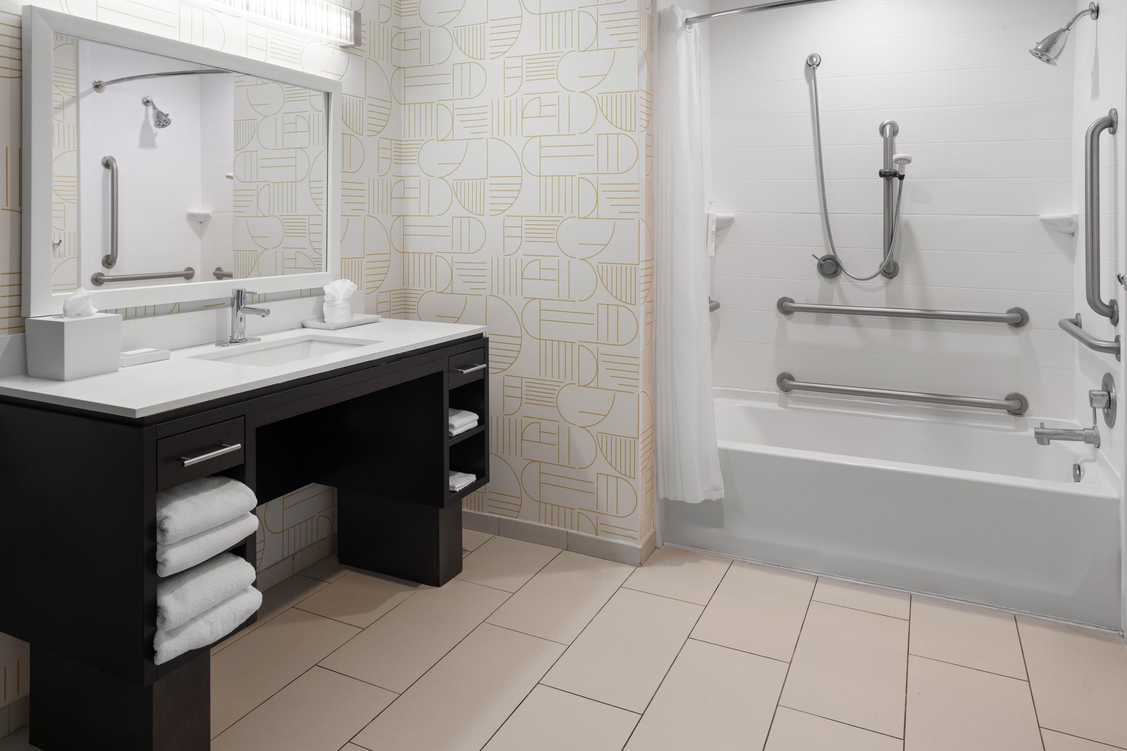 A modern bathroom with a double sink vanity, a shower with grab bars, and patterned wall tiles.