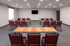 Une salle de conférence dotée d’une grande table et de chaises, d’un sol recouvert de moquette et d’un téléviseur à écran plat fixé au mur.