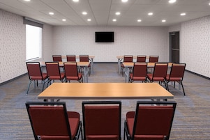 Un salón de conferencias con una gran mesa y sillas, piso alfombrado y un televisor de pantalla plana en la pared.