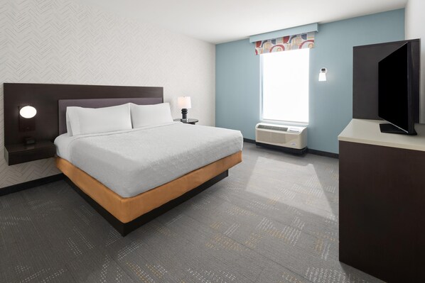 A hotel room with a bed, a bedside table with a lamp, a radiator, and a television.