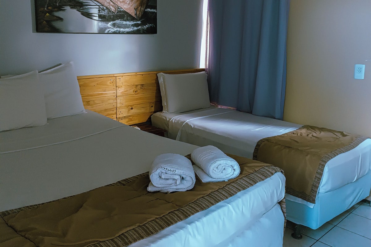 Habitación de hotel con cama, una cama adicional, un cuadro, aire acondicionado y ventana con cortinas.