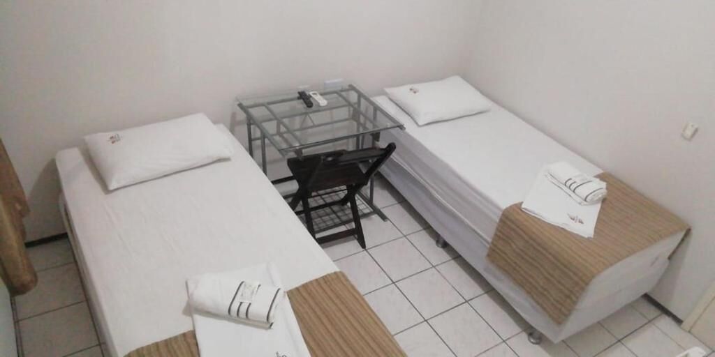 Una habitación pequeña y limpia con dos camas individuales, un escritorio y una silla.