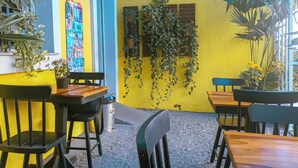 Un café aux murs jaunes, avec des tables en bois et des chaises noires.