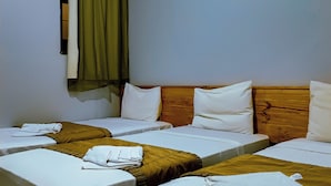 Une chambre d’hôtel avec quatre lits simples, une tête de lit en bois, une fenêtre avec des rideaux et un appareil de climatisation.