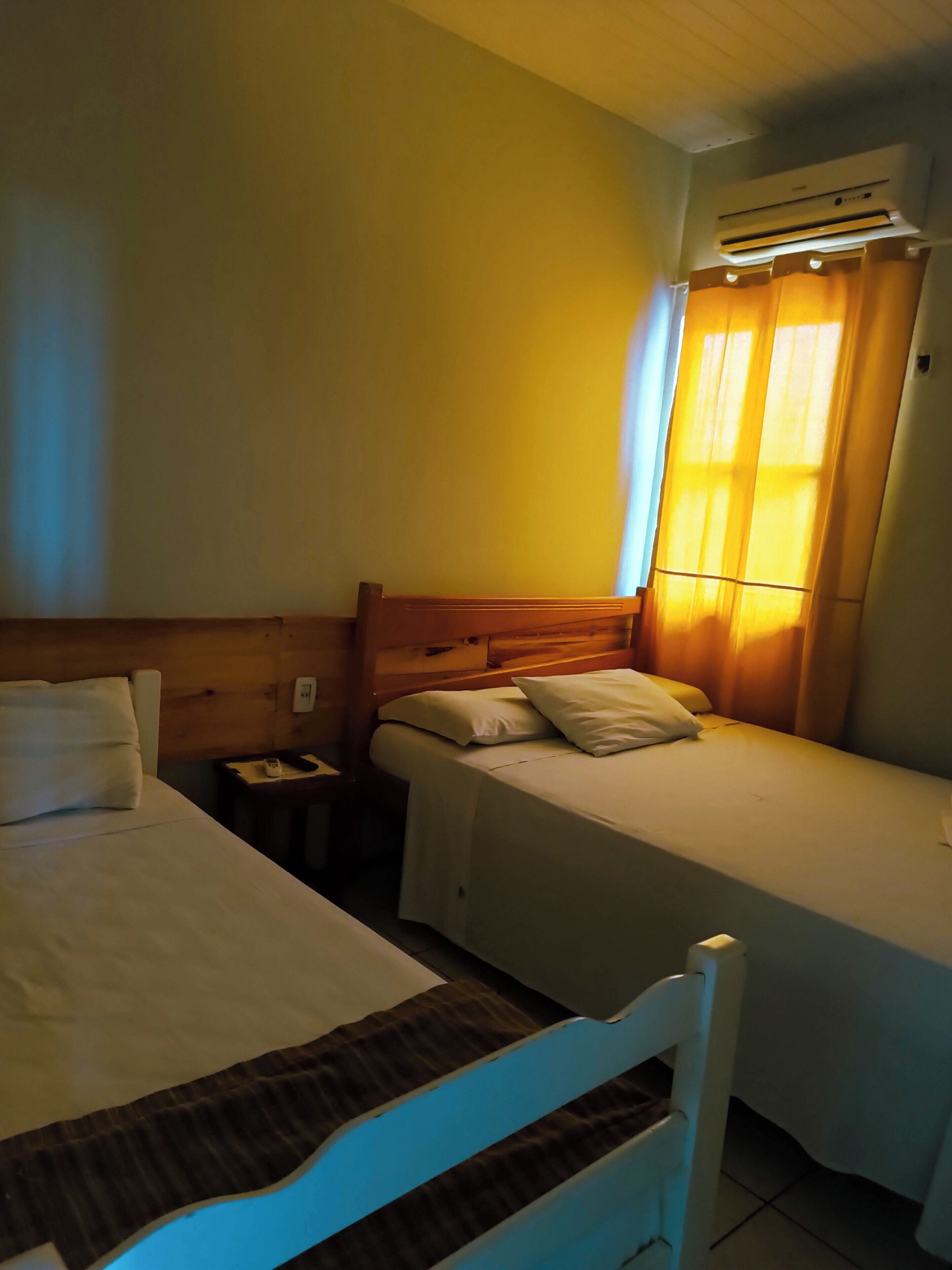 Habitación con dos camas, una mesita de noche, un aire acondicionado y una ventana con cortinas.