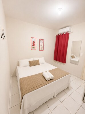 A hotel room with a bed, a red curtain, a wall-mounted air conditioner, and two framed pictures. - Center 1 Hotel (Fortaleza)