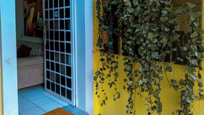 Un bâtiment jaune avec une porte blanche, une fenêtre à carreaux et un petit boîtier électrique fixé au mur.
