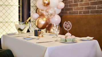 Una mesa dispuesta para un evento formal, con mantel blanco, platos, cubiertos y un pastel con un adorno decorativo.