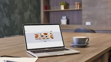 Ein Laptop auf einem Holztisch mit einer Kaffeetasse und einem Notizbuch.