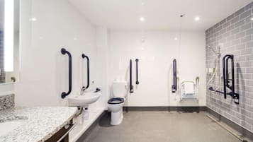 A modern bathroom with white tiles, a granite countertop, a white sink, a toilet, and a bidet.