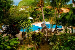 A pool surrounded by lush greenery and palm trees, with lounge chairs and umbrellas. - Pousada Arriba Pipa (Tibau do Sul)
