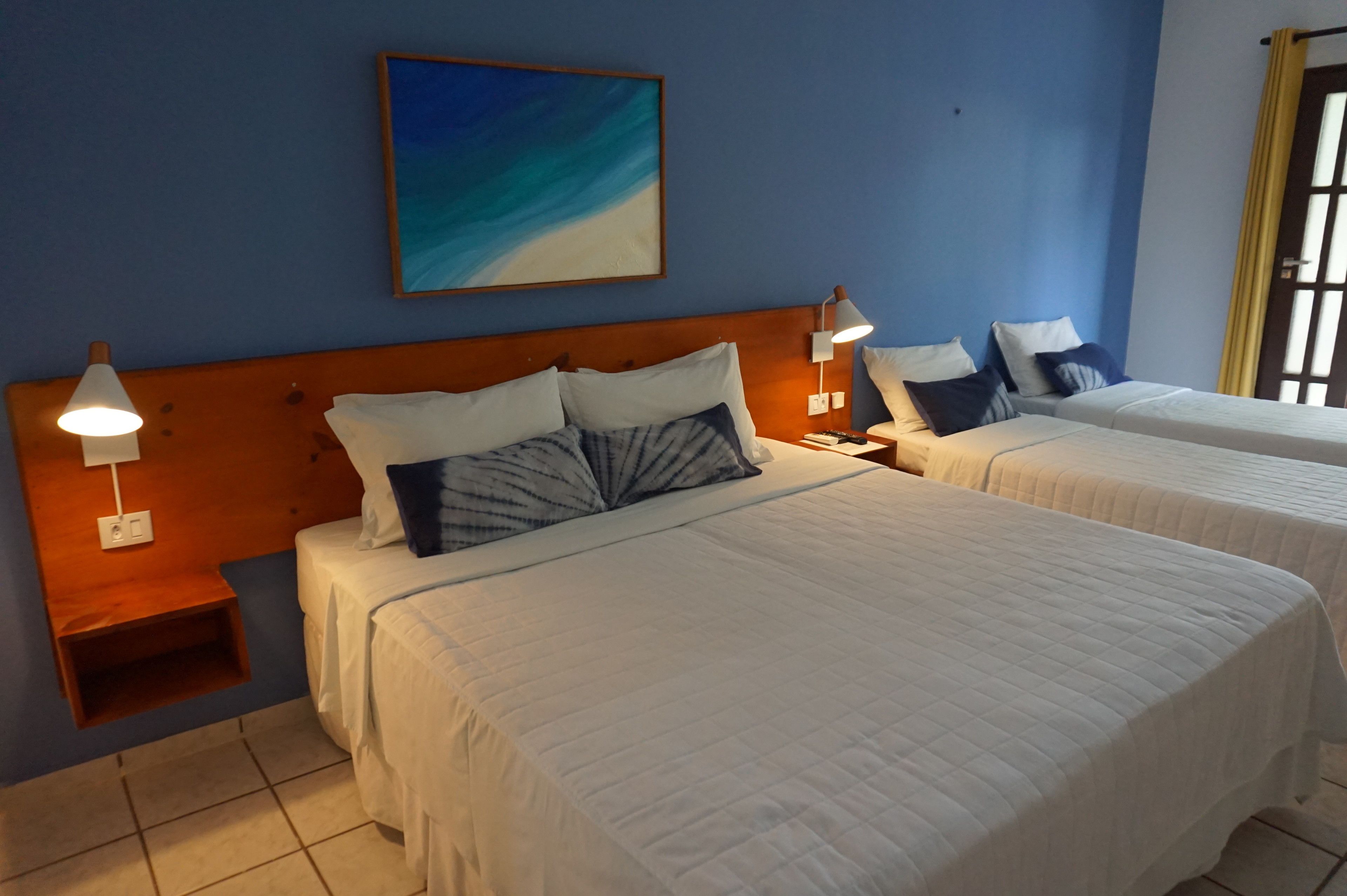 A hotel room with two beds, a wooden headboard, a painting on the wall, and a window with curtains.