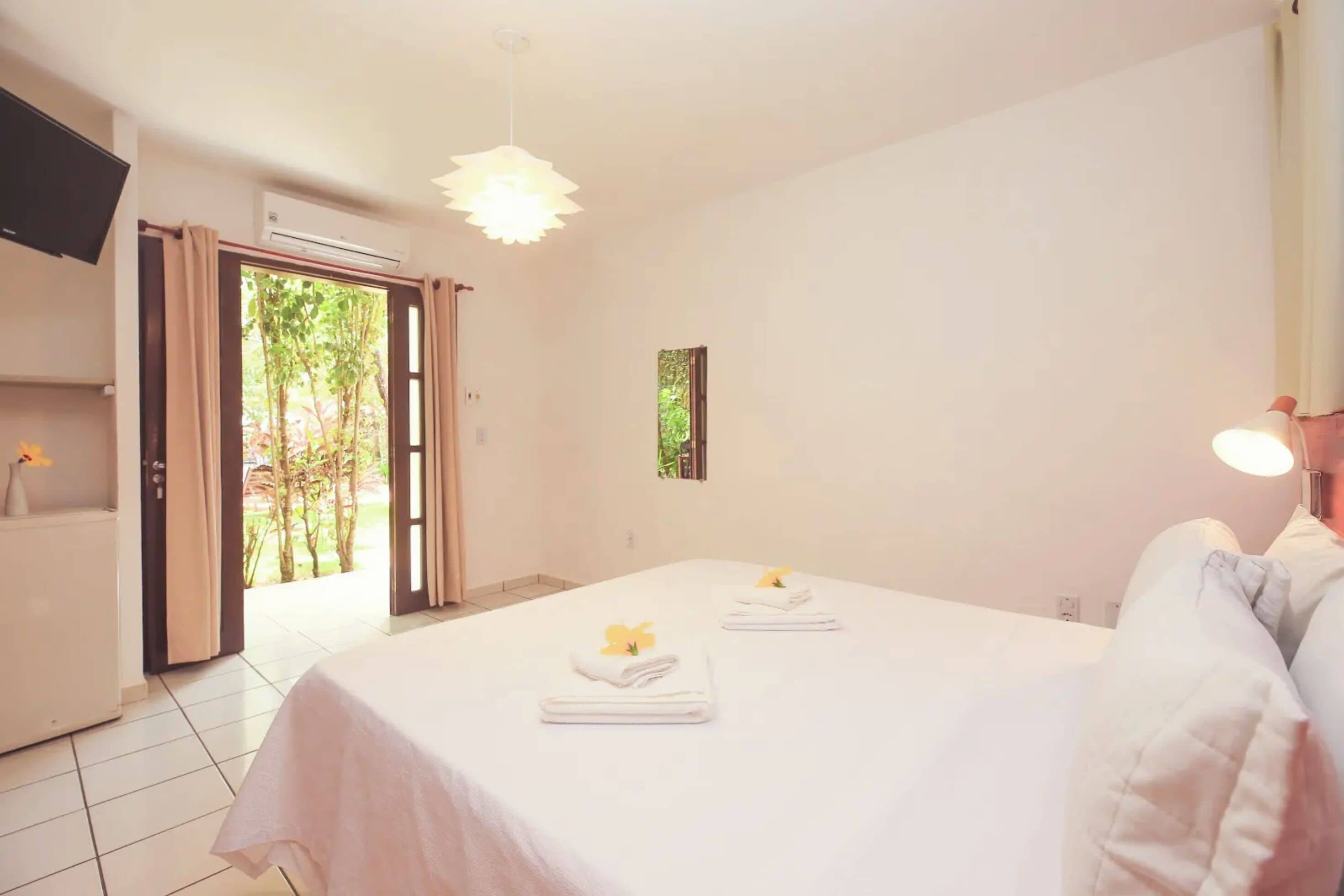 Una habitación de hotel con cama, televisión, aire acondicionado y puerta que da a un jardín.