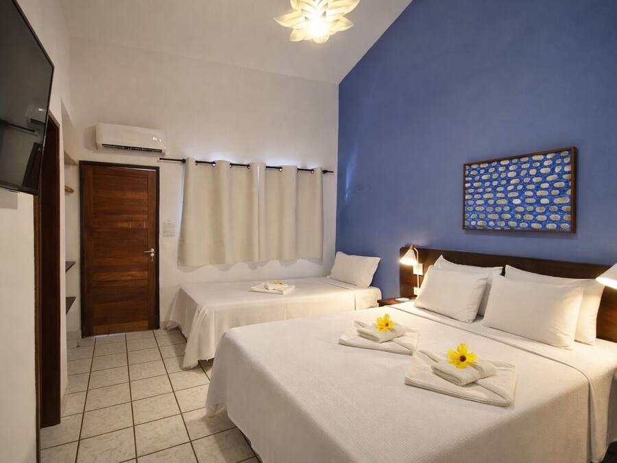 A hotel room with two beds, a TV, an air conditioner, and a blue accent wall.