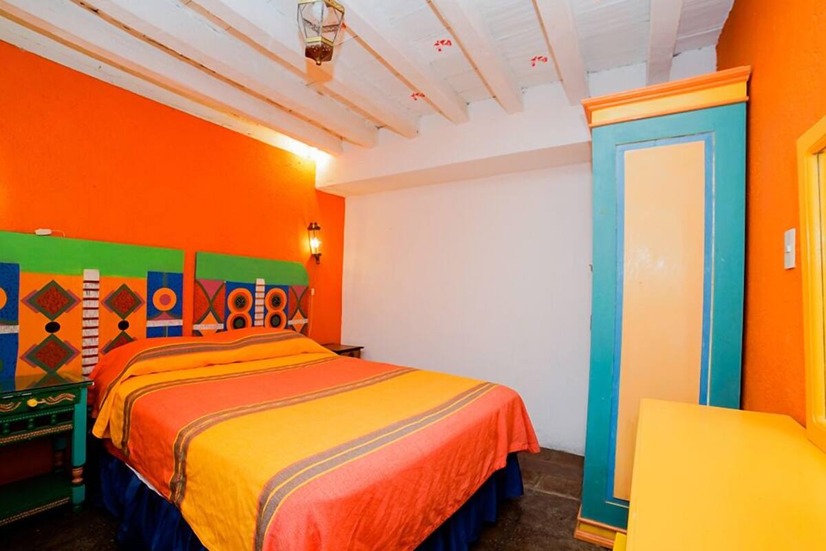 A room with a bed, a nightstand, a wardrobe, and a wall with colorful geometric patterns.