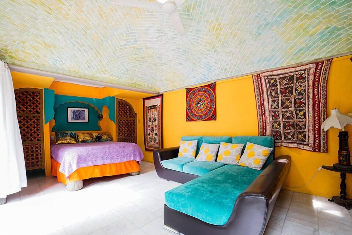 A room with a bed, a sofa, a patterned tapestry, and a lamp.