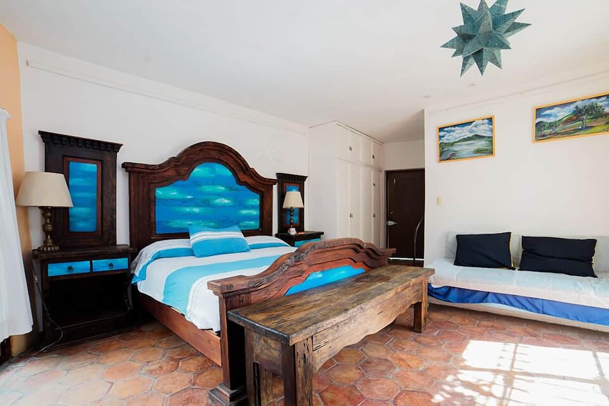 A bedroom with a large bed, a wooden bench, a nightstand, and a sofa.