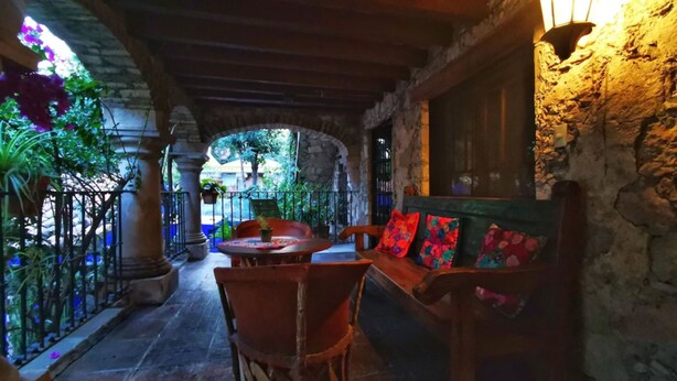 Un patio al aire libre con columnas de piedra, un banco de madera con cojines coloridos y un farol.