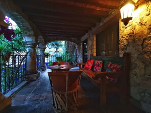 Un patio al aire libre con columnas de piedra, un banco de madera con cojines coloridos y un farol.
