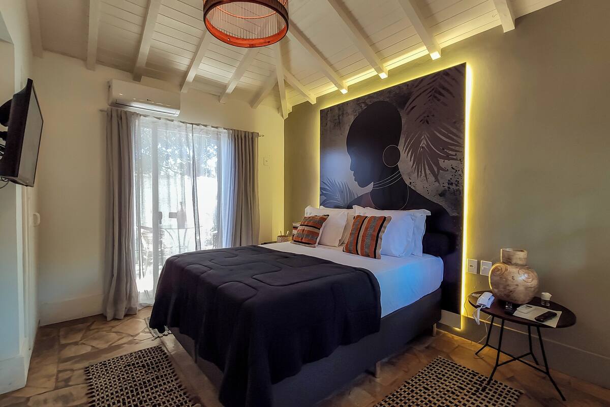 Un dormitorio con una cama grande, un televisor de pantalla plana, una lámpara fijada a la pared y un ventanal con cortinas.