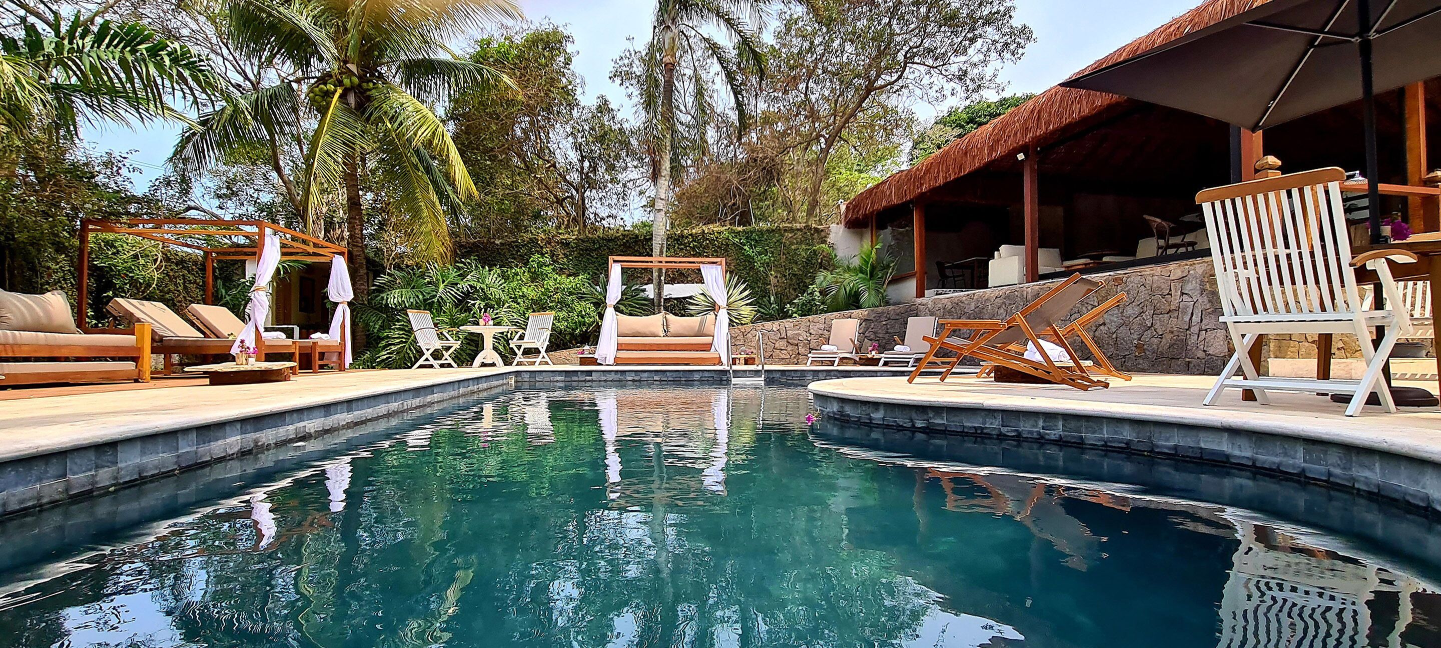 Uma área de piscina com espreguiçadeiras, um deck de madeira e um edifício com telhado de palha.