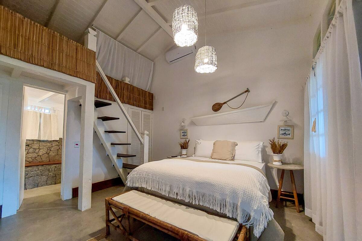 Un dormitorio con una cama grande, un banco de madera, una escalera y una lámpara colgante.