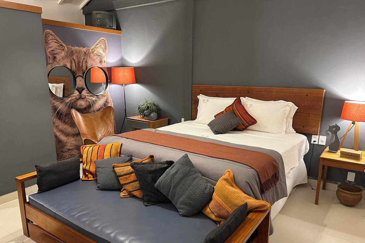 Un dormitorio moderno con una cama grande, cabecera de madera, una mesita de noche con lámpara y un espejo en la pared.