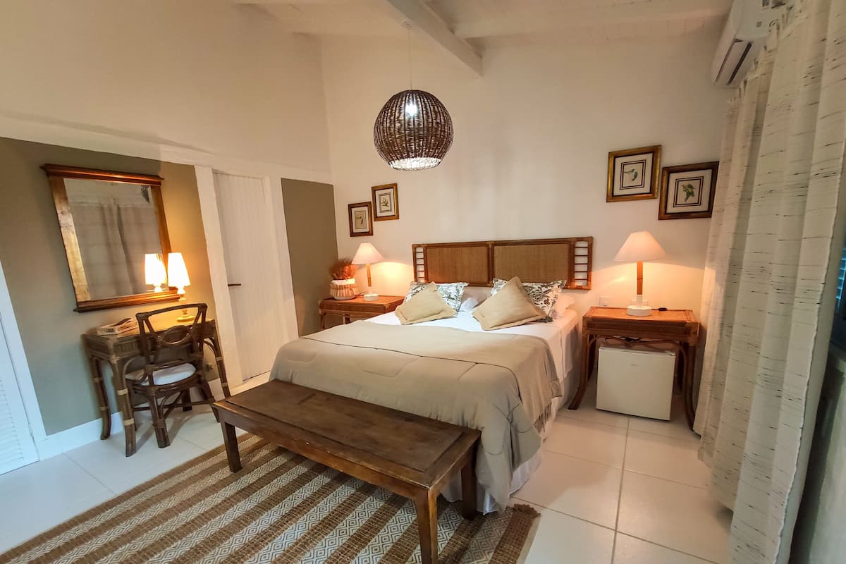 Un dormitorio con cama, mesitas de noche, escritorio, silla, lámpara colgante y un refrigerador pequeño.