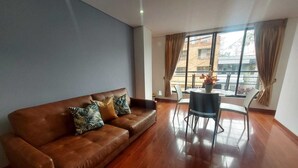 A modern living room with a brown leather sofa, a dining table with chairs, and large windows with curtains. - Luxury Suites & Apartments (Bogotá)