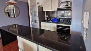A modern kitchen with a black countertop, white cabinets, a microwave, and a gas stove. - Luxury Suites & Apartments (Bogotá)