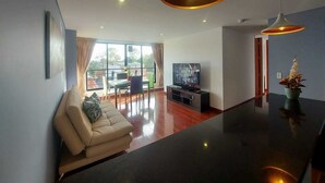 A modern living room with a sofa, a TV, and a dining area with a table and chairs. - Luxury Suites & Apartments (Bogotá)