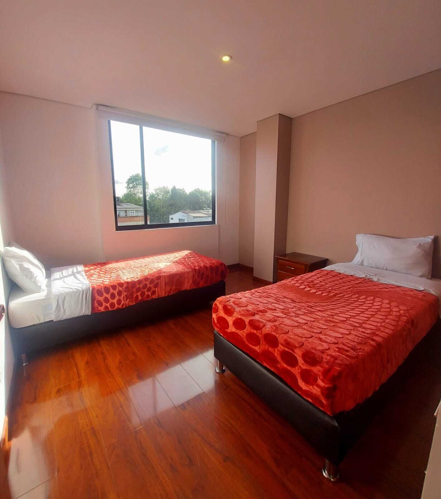 A hotel room with two beds, a large window, wooden flooring, and a white chair.