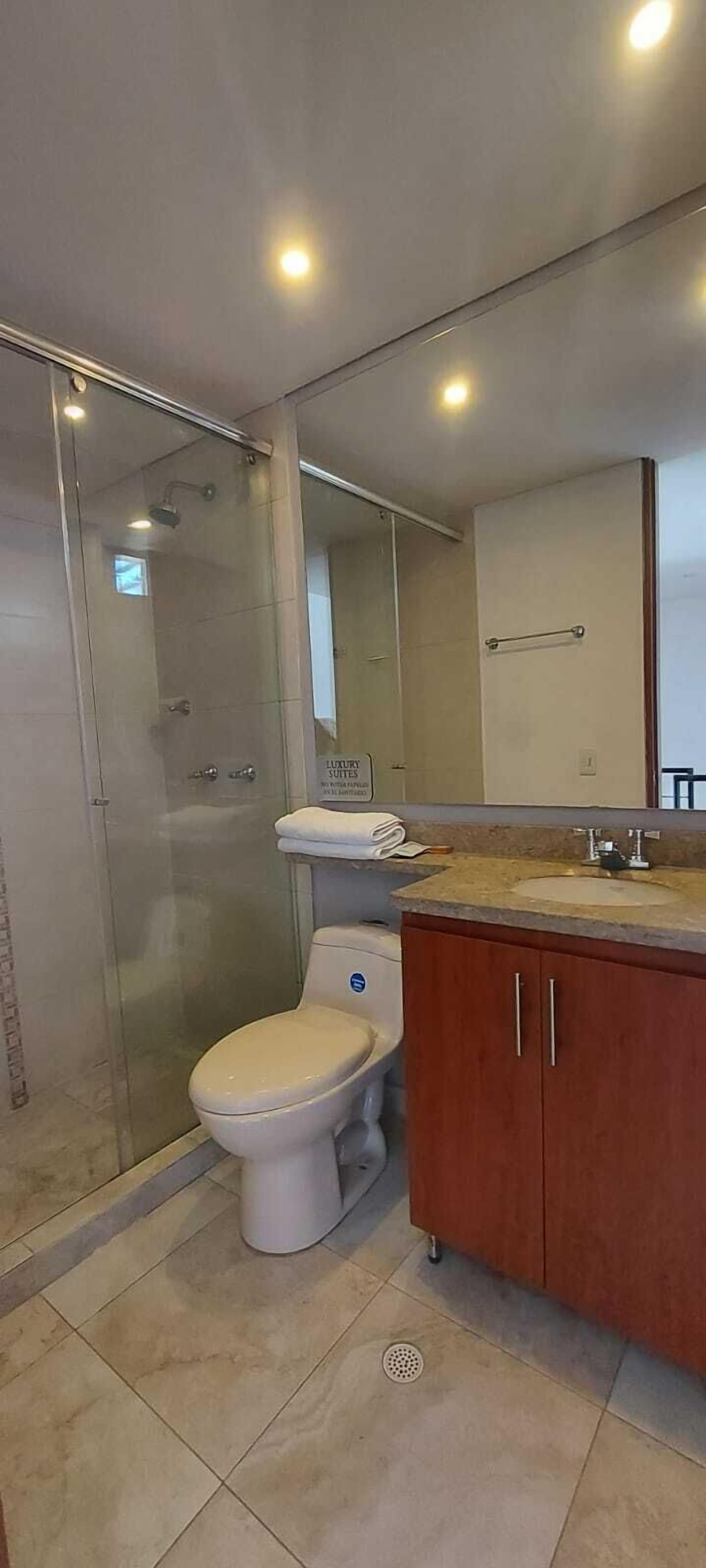 Un baño moderno con ducha de vidrio, inodoro, lavabo y tocador con armarios.
