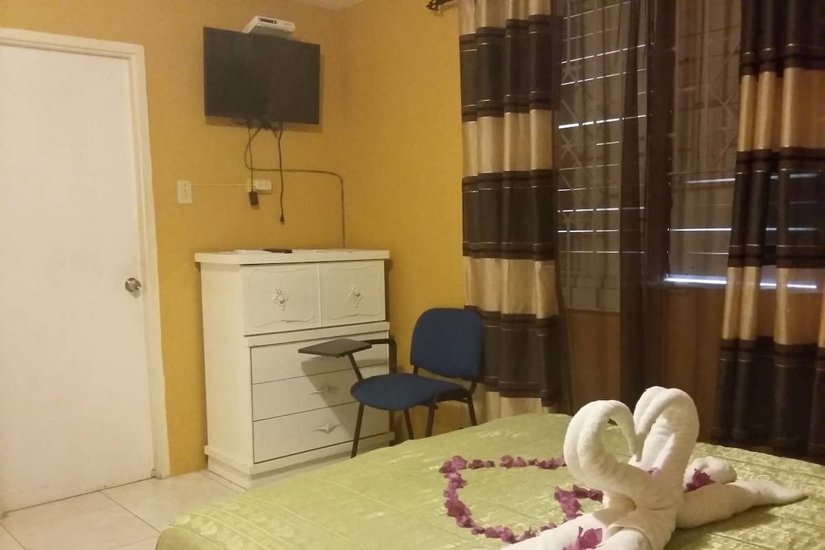 A room with a bed, a dresser, a chair, a television mounted on the wall, and a window with curtains.