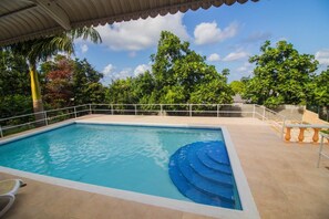 A rectangular pool with a blue edge, surrounded by a white railing, and a covered area with a curved roof.