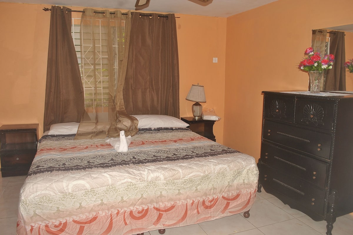 A bedroom with a bed, a dresser, a nightstand, a lamp, and a vase with flowers.