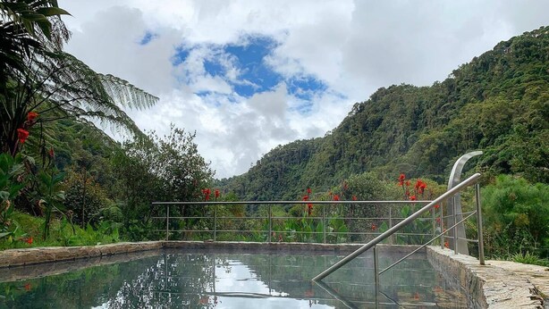 Ein ruhiger Pool im Freien mit Metallgeländer, umgeben von üppiger Vegetation und einer Bergkulisse.
