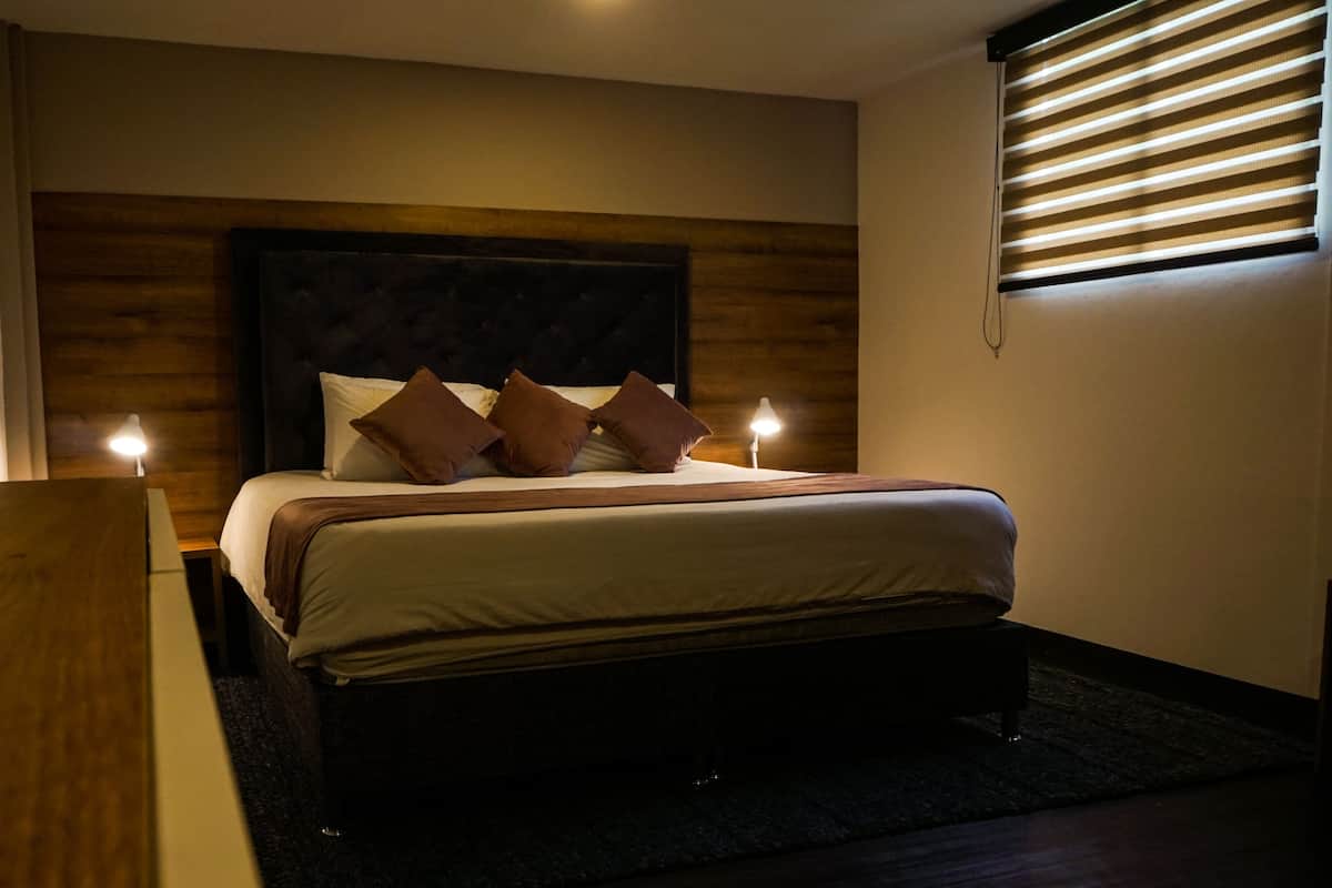 A hotel room with a wooden headboard, a bed with white linens and brown pillows, two bedside lamps, and a wooden nightstand.
