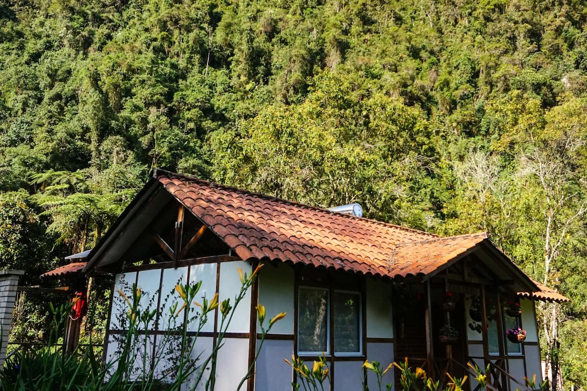 A traditional building with a tiled roof, surrounded by lush greenery and a forested hillside.